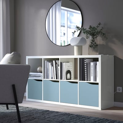 KALLAX shelf with blue door, books, lamp, plants. Under mirror, beside armchair.