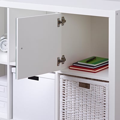 White KALLAX shelf with mirror door open, displaying stacked books on top shelf, woven basket at bottom.