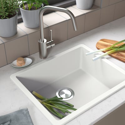 Modern kitchen sink with stainless tap, green onions, and potted herbs.