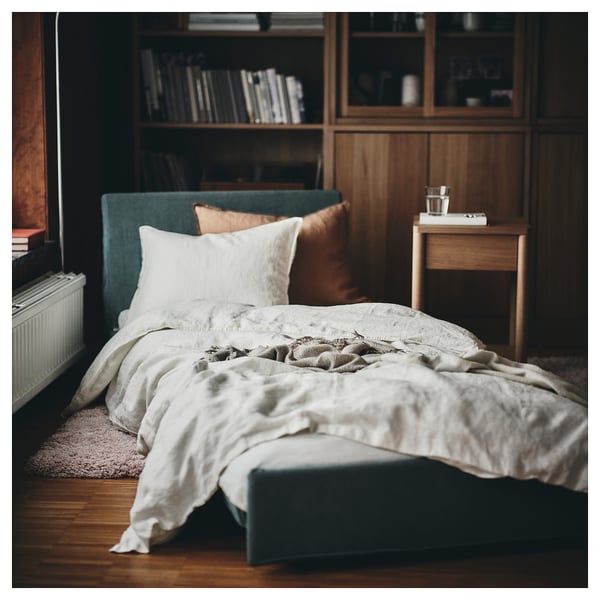 Unmade KIVIK sofa with green blankets and bookshelf.