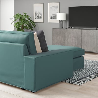 Modern living room with KIVIK teal sofa, grey rug, tv, lamp, art, and green plant.