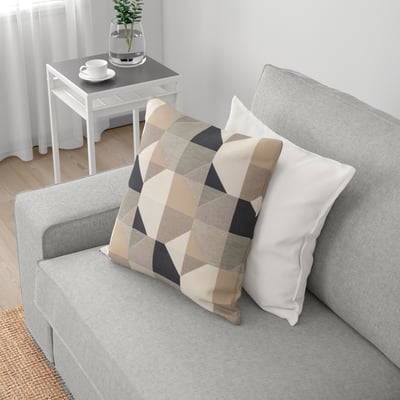 Modern living room with KIVIK sofa, light grey with chequered and white pillows. Small side table with mugs and plant.