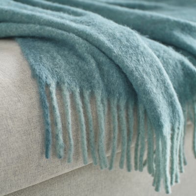 A soft, light turquoise throw draped with fringe texture, showing a cosy, fluffy feel.