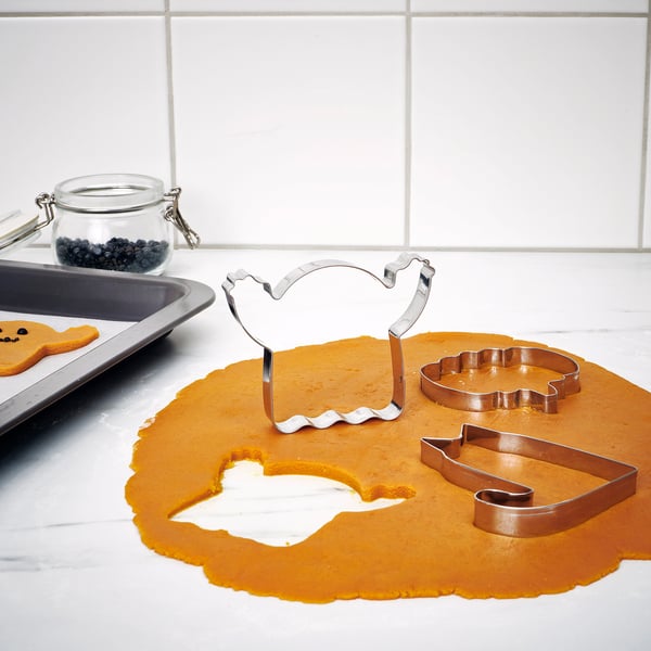 Cookie cutters on orange dough, with gingerbread person and berries.