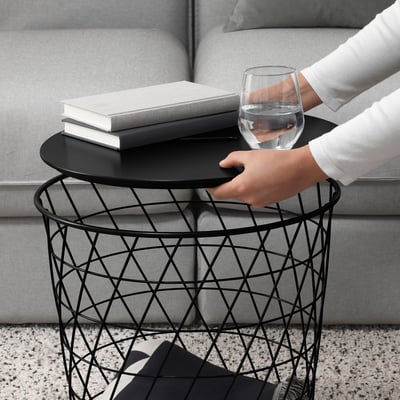 A person holding a modern metal side table with a glass of water and books, showcasing its portability and storage functionality.
