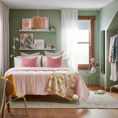 A bed with a soft, light pink comforter, neatly folded, and a small white notebook on top, showcasing a cosy and well-made sleeping environment.