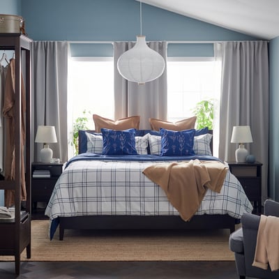 LINSNÄRJA blue chequered bedding set. Centred on bed with brown pillows, flanked by lamps. Matched nightstands and wardrobe, grey curtains.