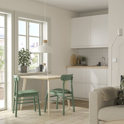 Modern compact dining set with white table, green chairs, white kitchen backsplash, and a couch.