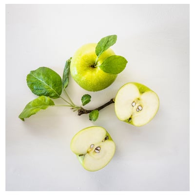 Three green apples, one whole, two cut; leaves attached, on grey surface.