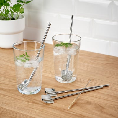 Glasses of water with ice, mint, and straws, plus cleaning brush and spoon straws on wood.