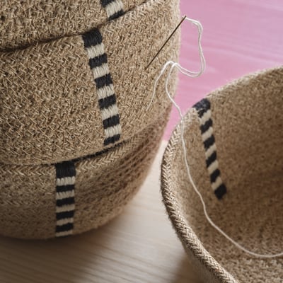 Handwoven jute basket with black-white thread patterns. Threaded needle seen, showcasing craftsmanship and texture.