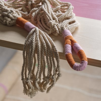 Handmade macramé plant hanger, featuring intricately knotted natural cotton cords, displayed on a wooden shelf.