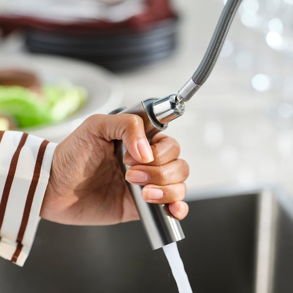Person holding MAJSJÖN kitchen tap with dual-spray feature. High-quality stainless steel spout, smooth water flow.