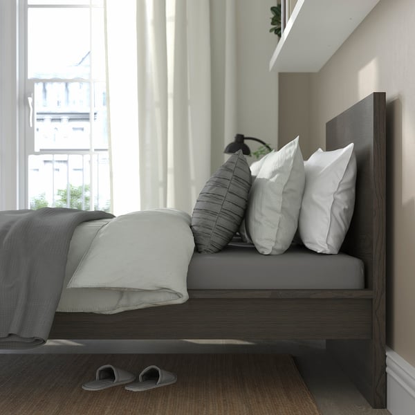 Modern bedroom with bed, large windows, clean design. Bed has high headboard, supportive slats, adjustable sides. Slippers underneath.