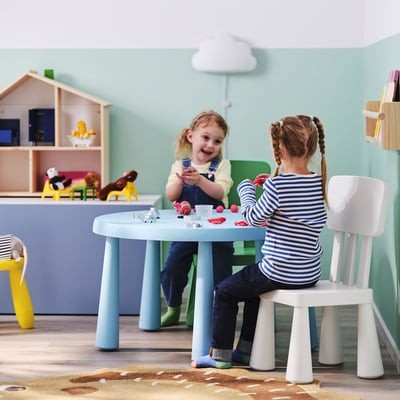 Kids playing with toys at blue table, kitchen in background.