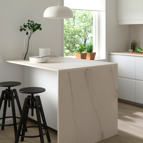 Modern kitchen with MÖCKLARP porcelain worktop, stacked dishes, vase, pendant lamp, large window.