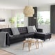 Modern living room with black leather l-shaped sofa, wooden side tables, white rug, and large window. A stylish and cosy setup.