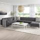 Modern living space with large grey l-shaped sofa, white coffee table, and tall curtains. Large windows with a scenic view.