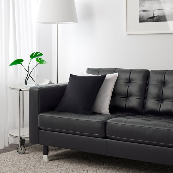 Modern living room with black leather sofa, pillows, plant, and lamp.