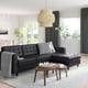 Modern living room with black leather l-shaped sofa, black & white pillows, wooden tables, area rug, plants, large window, and hanging light fixture.