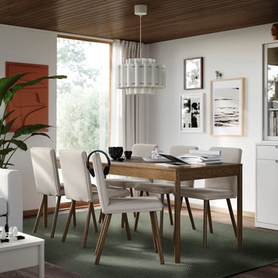 Modern dining room with MORUM rug, wooden table, beige chairs, flowers, chandelier, artwork, clock, window, plant, cabinet.