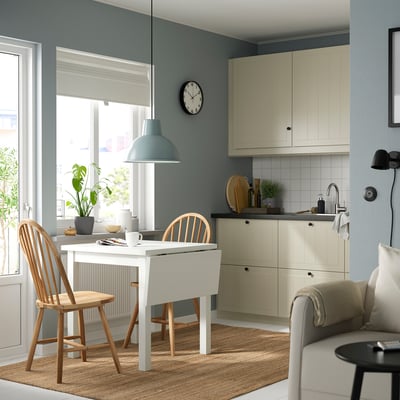 Modern kitchen with NORDVIKEN table, chairs, blue pendant light, and black clock. Beige sofa with light blue walls and potted plant.