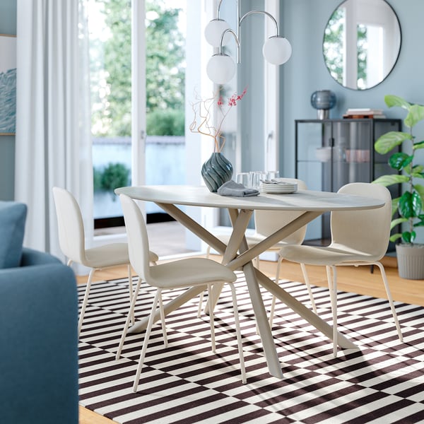 Modern minimalist dining setup with norrmjölle white oval table and chairs. Light wood, geometric rug. Bright, airy room with large windows.