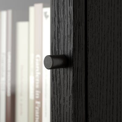 Dark wooden handle on glass-fronted cabinet, showcasing craftsmanship and modern design.