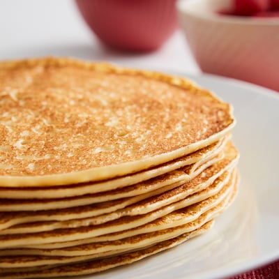 Stack of golden-brown pancakes on a white plate, ready to be served.