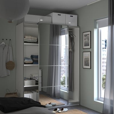 Modern bedroom with a white PAX wardrobe featuring mirrored sliding doors, grey curtains, and neatly folded clothes on visible shelves.
