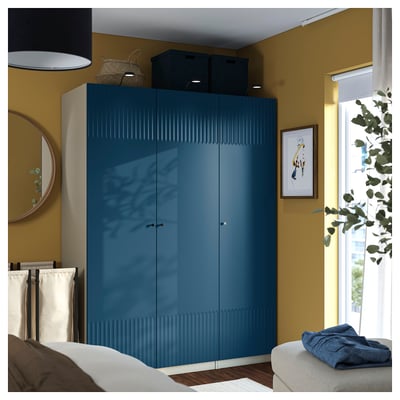 Blue PAX wardrobe near ceiling, sleek design, mirror left, plant right, bed with bedding, towel, picture on wall, natural light.