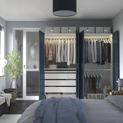 Modern bedroom with PAX wardrobe, hanging clothes, shelves, drawers, and soft lighting.