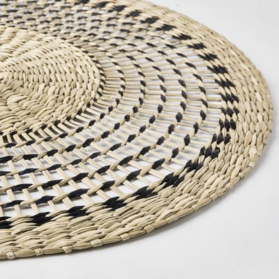 Handwoven round place mat, featuring intricate black and natural sedge patterns, offering a rustic yet elegant dining experience.