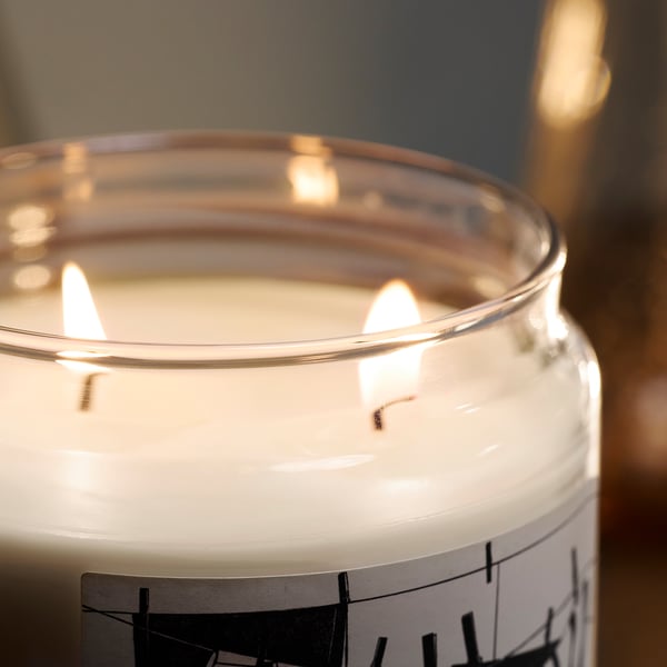 Burning candle in glass jar, white wax, dual wicks, gentle light and scent.