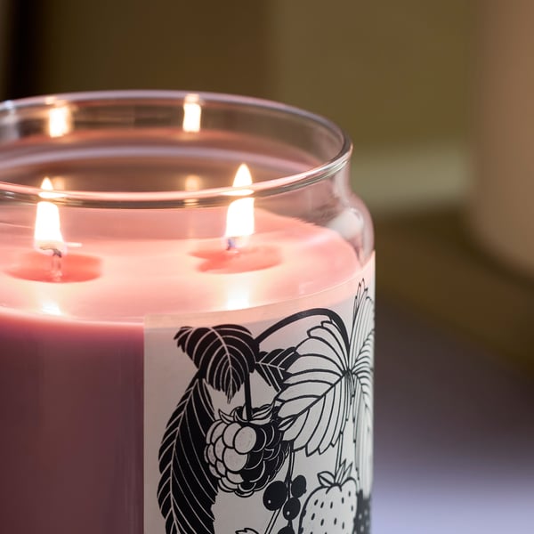 Three-wick scented candle in glass, red wax, emitting warm glow.