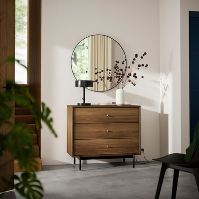 Modern bedroom with RÅDMANSÖ dresser - walnut, 3 drawers, black legs, round mirror, dried flowers in vase.