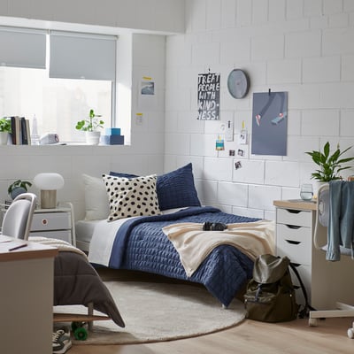 Cosy bedroom with dark blue RÄVSTARR bedding, fluffy comforter, and polka dot pillows. Twin bed by large window, warm atmosphere.