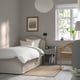 Cosy bedroom with RAMNEFJÄLL bed, small bedside table, lamp, books, wicker chair, plant.