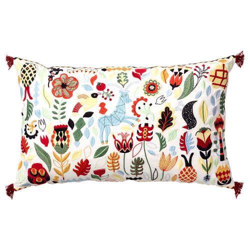 A rectangular white pillow with multicoloured floral patterns, tassels, and embroidered details in red and green.