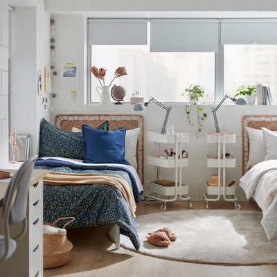 Serene blue floral comforter on large bed, wicker headboard, white room with large windows.