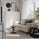 Modern living room with beige sofa, side table, plants, lighting, white cabinet, clock, art, and large window with sheer curtains.