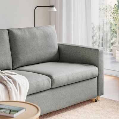 A grey sofa with a plush, removable cover sits by a window, providing comfortable seating and a smooth, easy-to-use sofa-bed mechanism.