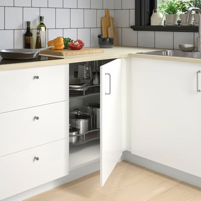 Modern kitchen with organised corner cabinet, wooden counter, fresh veggies, grey backsplash, stainless sink.