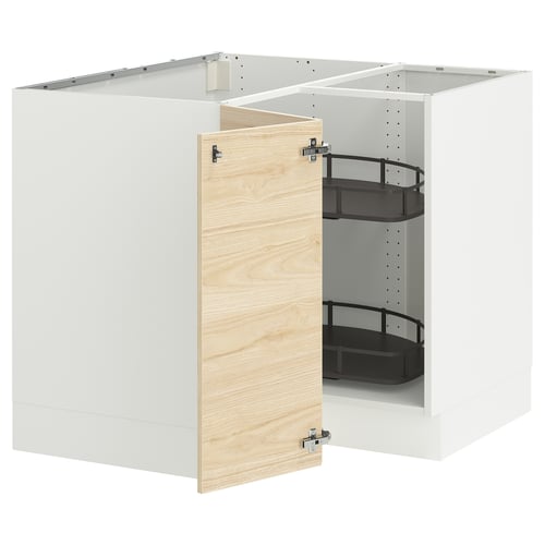 A white corner base cabinet with an open door from IKEAs SEKTION kitchen system. It a light ash wood-patterned door and two black shelves inside.