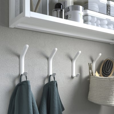 White double hooks on wall with towels hanging, shelf above with bathroom items.