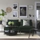 Modern living room: sleek emerald sofa, black coffee table, soft rug. Wall framed art, green plant. Cosy, minimalist, inviting.