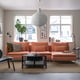 Modern living room: orange sectional, soft cushions, white pendant lamp, black coffee table, city view.