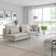 Modern living room with grey l-shaped sofa, cushions, coffee table, large windows, and flowers.