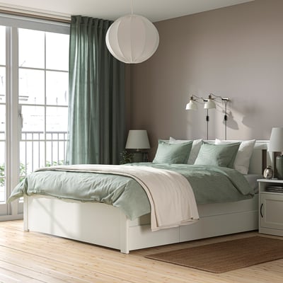 A modern bedroom with a white SONGESAND bed, soft bedding, side tables, and a large window with green curtains.