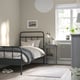 Bedroom with STJÄRNÖ black bed, curved headboard, and wooden floor. Includes bedside table, lamp, plant, and decor.
